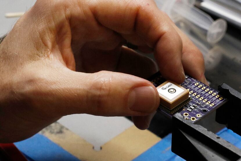 Jesse Hammer, chief engineer & co-founder of Kubos, places a GPS chip on a printed circuit...