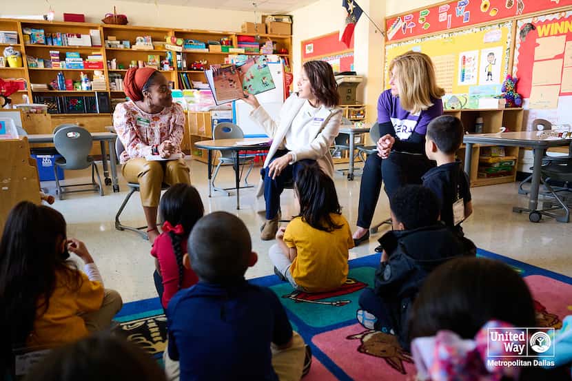 Three volunteers read to children sitting on a rug in an elementary school classroom.