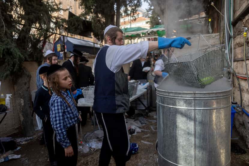 An ultra-Orthodox Jewish man dips cooking utensils in boiling water to remove remains of...