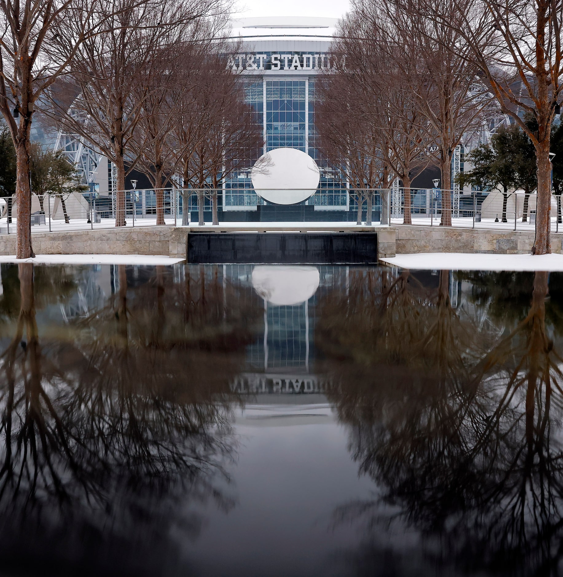 The frozen Sky Mirror sculpture outside AT&T Stadium is reflected in the water after a band...