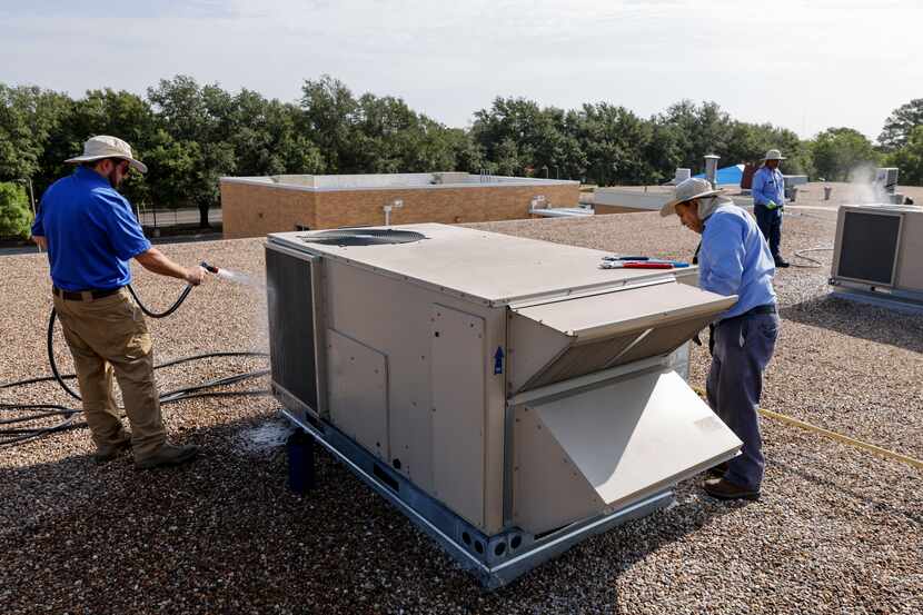 HVAC technician Armand Lajesse (left) cleaned the coils of an air conditioning unit on the...