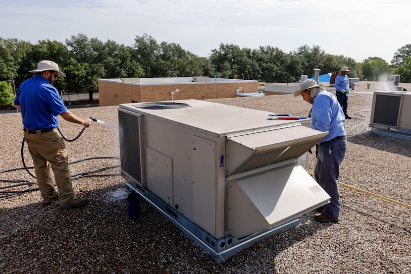 HVAC technicians clean the coils of an air conditioning unit on the roof of Wimbish World...