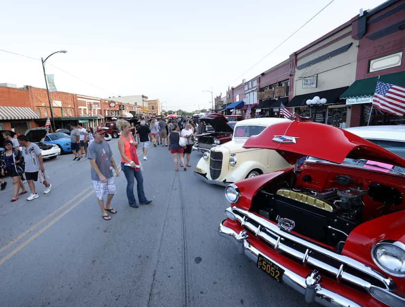 Guests stroll past classic cars on display during the Bluegrass on Ballard festival in Wylie...