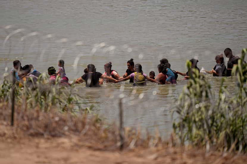Migrantes tomados de las manos cruzan el Río Grande cerca de donde colocaron boyas como...