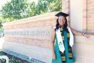African American woman wearing a graduation cap and sash poses in front of the University of...