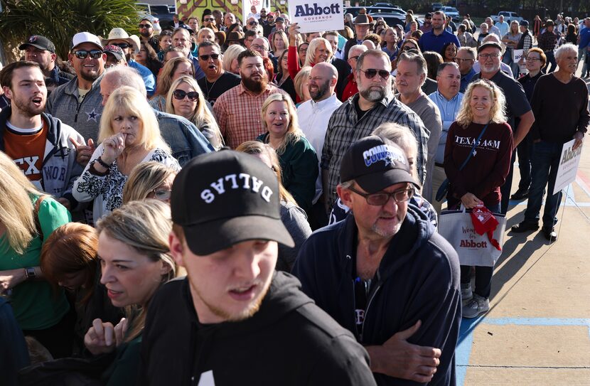 People wait in line to meet Gov. Greg Abbott as a protestor walks by them yelling, Tuesday,...