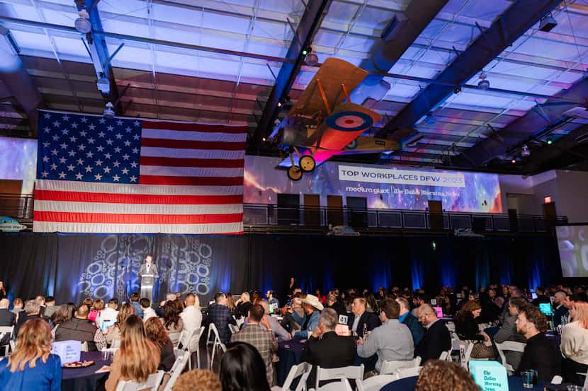 Interior view of Frontiers of Flight museum with a U.S. flag, a stage, and an audience...
