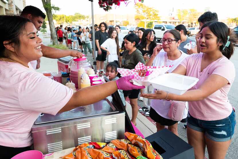 Aidee del Villar, left, owner of Me Enloteces, hands Mia Aleman, 13, an order of Takis Elote...