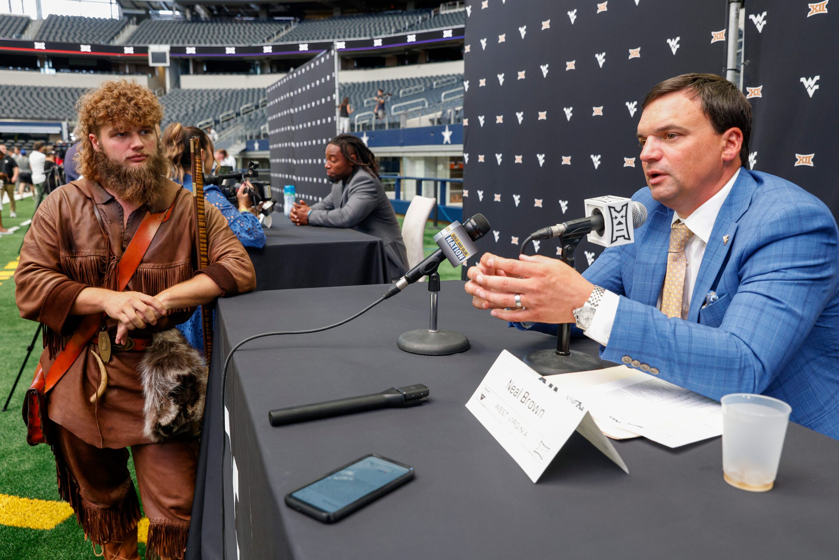 West Virginia Mountaineers mascot Mikel Hager listens as head coach Neal Brown talks with...