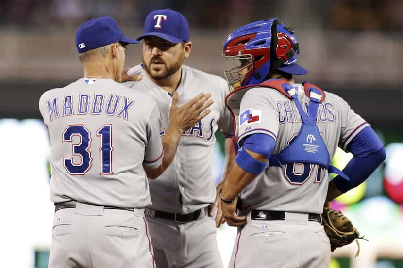 Texas Rangers pitching coach Mike Maddux, left, pats pitcher Joe Saunders, center, during a...