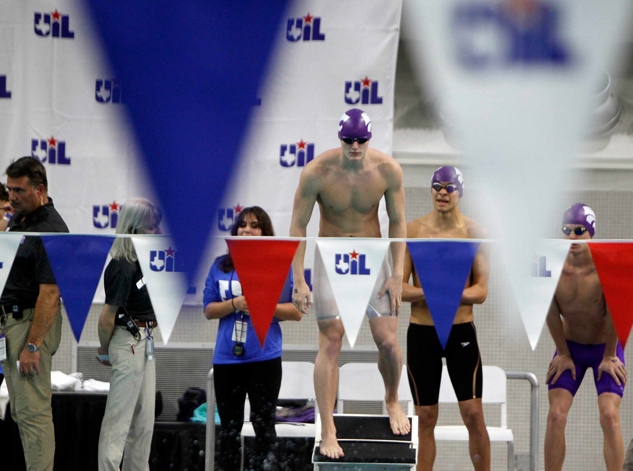 A swimmer is poised on the blocks behind a UIL flag draped across the pool during a 5A relay...