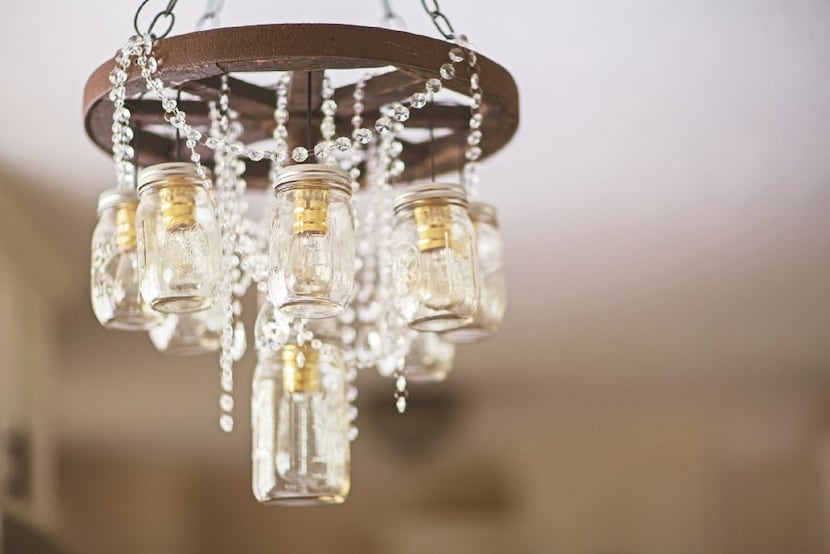 A wagon wheel and mason jar chandelier is dripping with crystals in a Junk Gypsy-designed...
