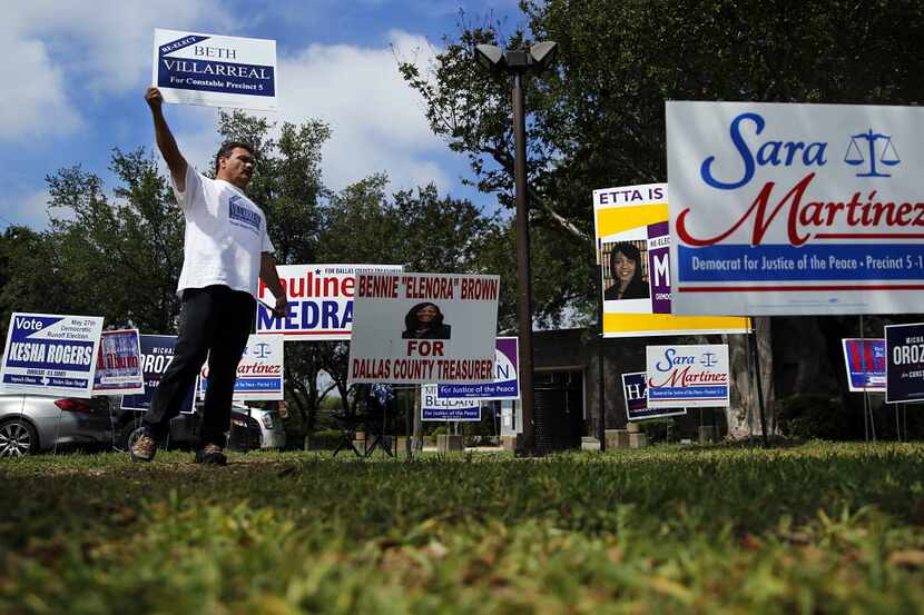 Volunteer Roman Gonzalez paces among an array of political signs covering the parking area...
