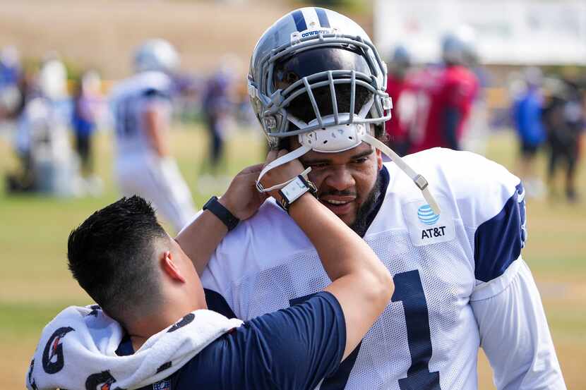 Dallas Cowboys tackle La'el Collins has his helmet worked on during a joint practice with...