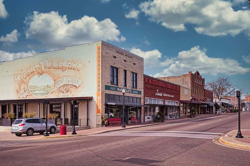 A wide shot of Historic downtown Mount Pleasant, TX, by day. A silver car is parked on the...