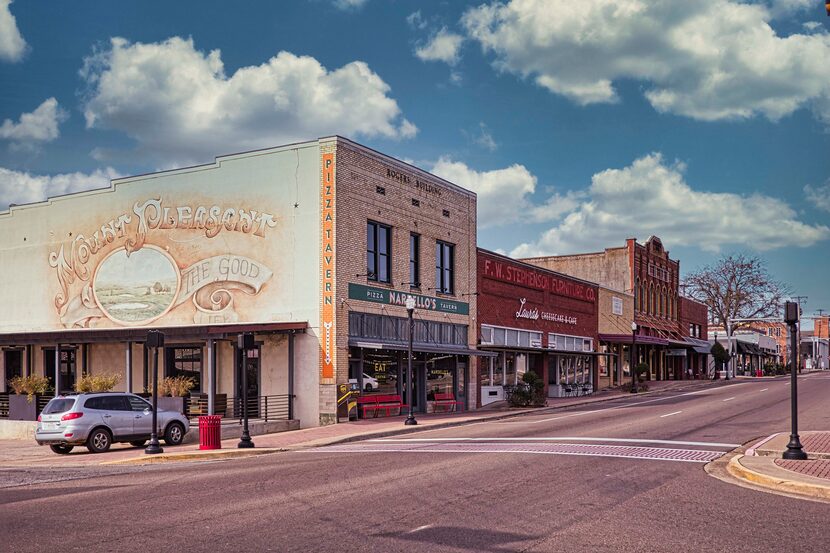 A wide shot of Historic downtown Mount Pleasant, TX, by day. A silver car is parked on the...