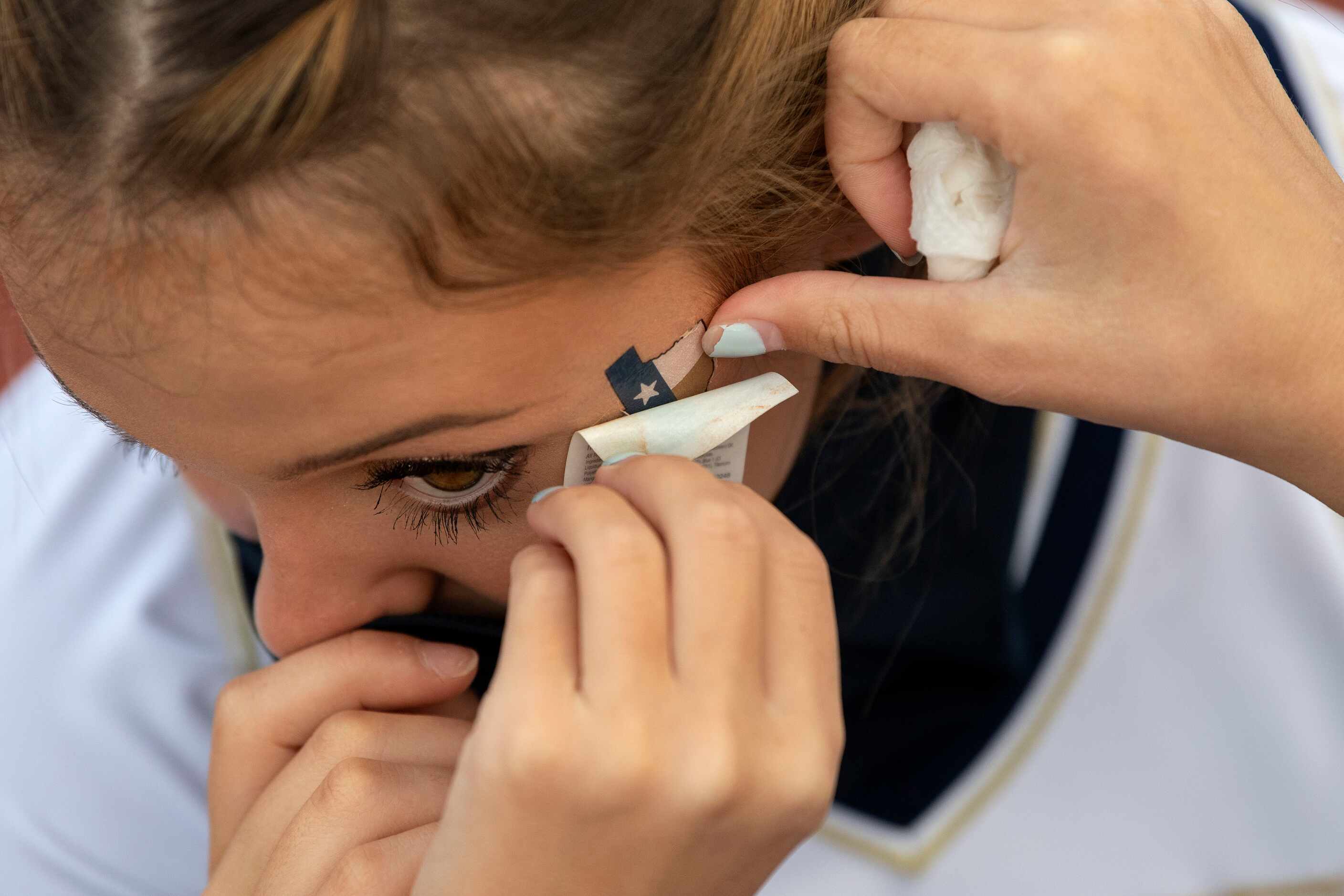 Jesuit junior cheerleader Elle De La Garza get some help applying a temporary tattoo before...