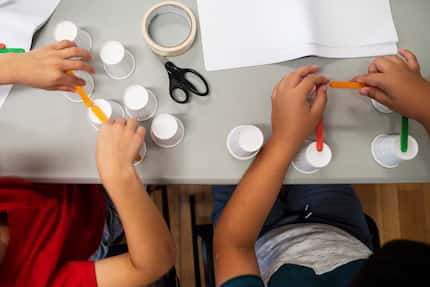Two young boys use a variety of items such as cups and popsicle sticks to build a bridge as...