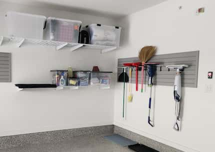 Garage with wall racks holding bins and slat wall with hanging cleaning equipment.