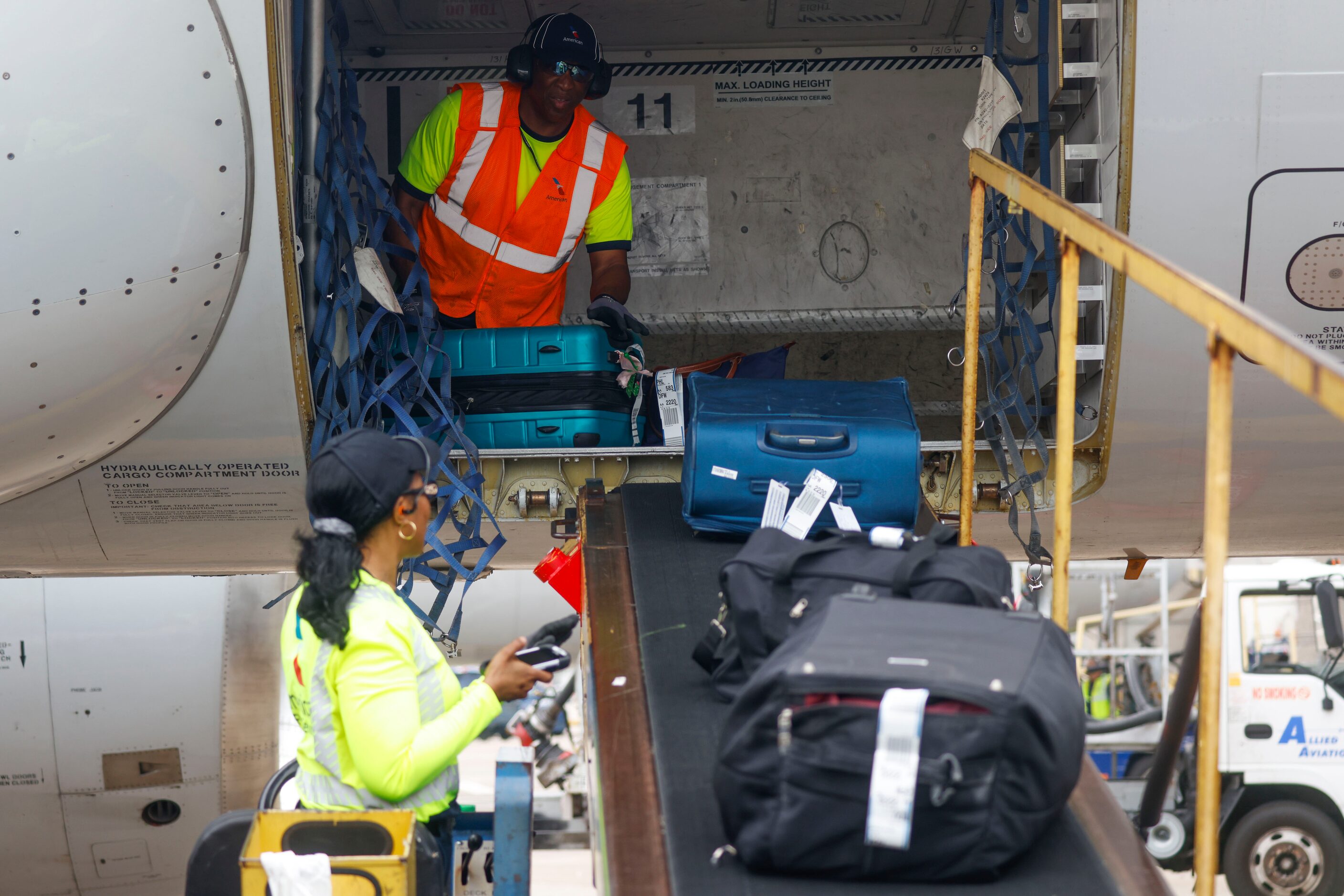 Members of the ground crew unload baggages from an American Airlines flight from Grand...