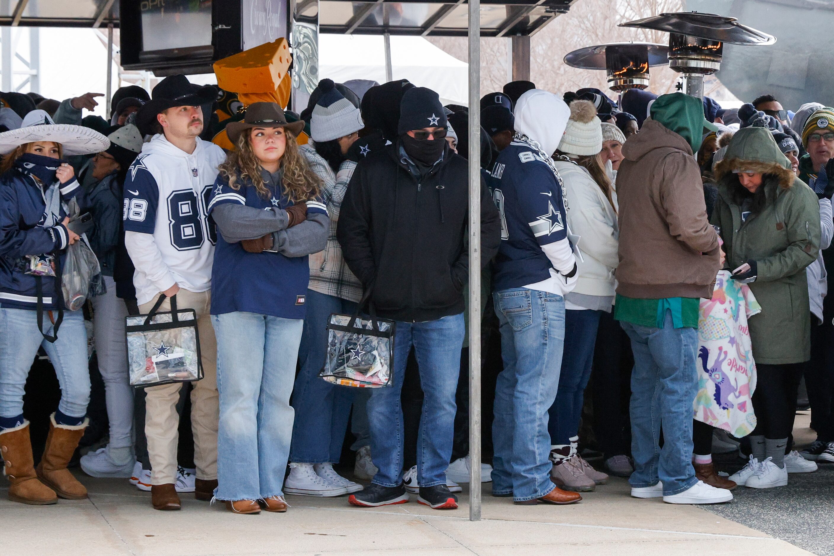 Fans gather under propane heaters with temperatures below freezing as they wait for doors to...