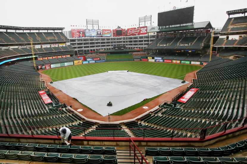 A stadium employee squeegees water in the seating area behind home plate during a rain delay...