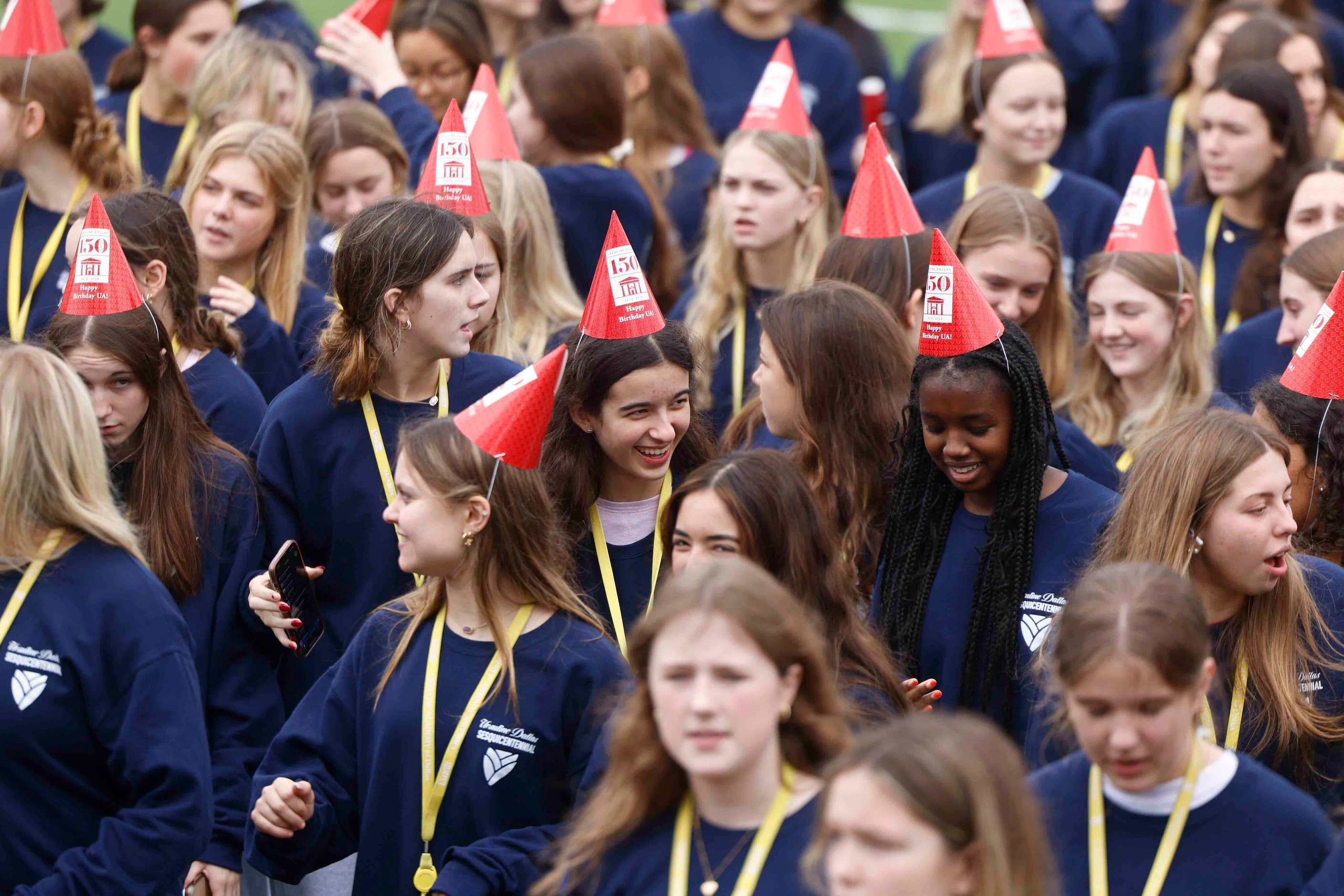 Students wearing birthday hats walk off the field after a giant group photo during the 150th...