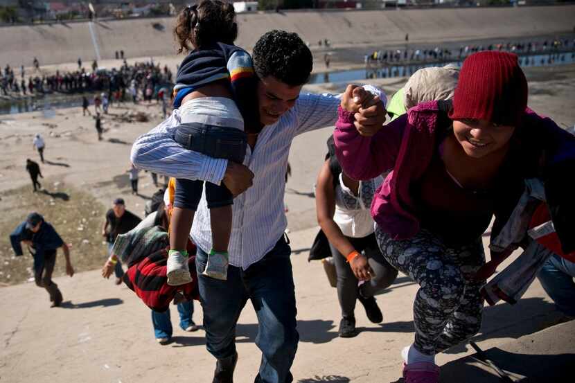 Migrants walk up a riverbank at the Mexico-U.S. border after getting past a line of Mexican...