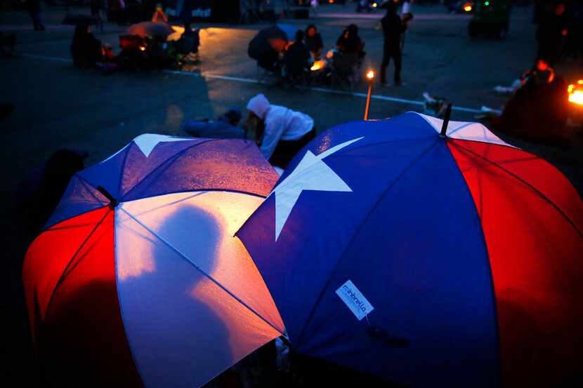 People take cover from the light rain under Texas flag umbrellas. (Tom Fox/Staff Photographer)