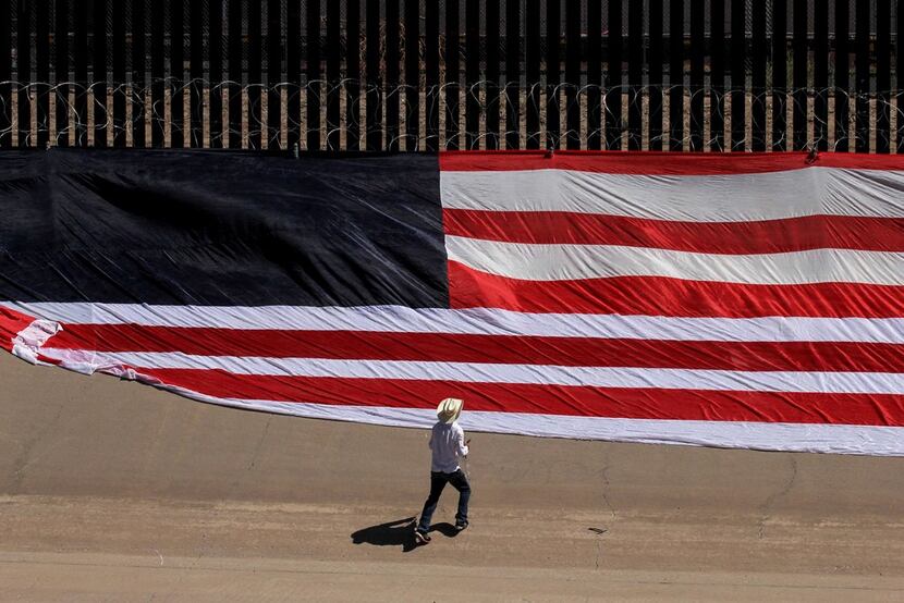 Mexican U.S. resident Roberto Márquez places a U.S. flag on the border fence next to Rio...