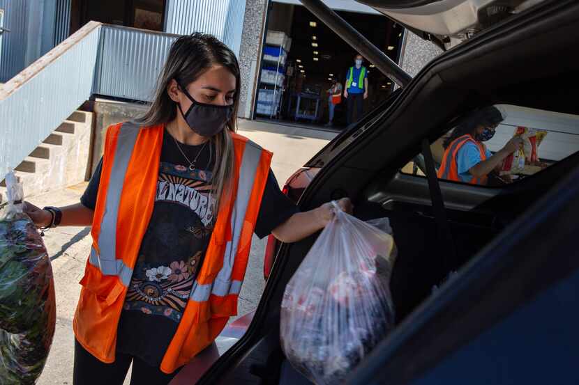 Andrea Ramirez from Crossroads Community Services, places bags of food into a client’s trunk...