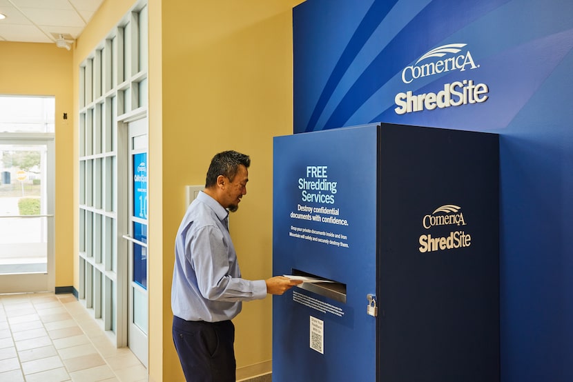 A man feeds a sheet of paper into a large locked box marked "Comerica Shredsite"