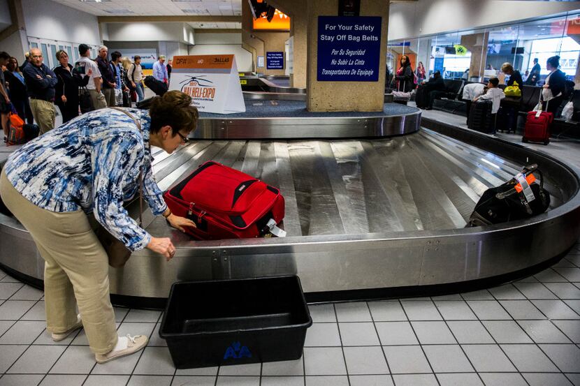 A traveler reaches for her bag as luggage moves around a baggage claim at Gate C on Friday,...