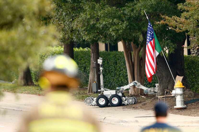 A suspicious package is pulled out of the bushes by a police robot in front of the...