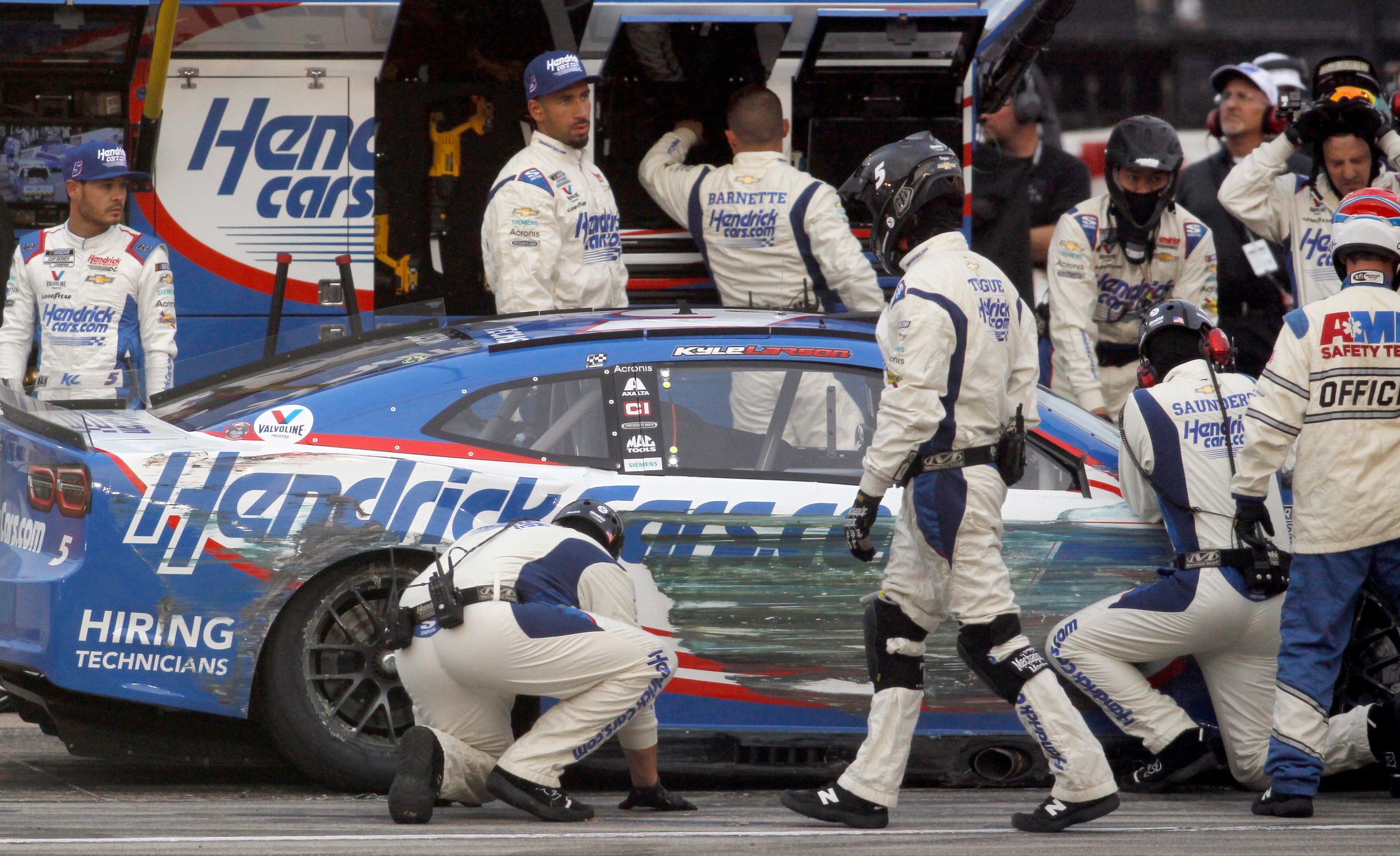 Driver Kyle Larson, left, watches as his pit crew assess the damage to his #5...