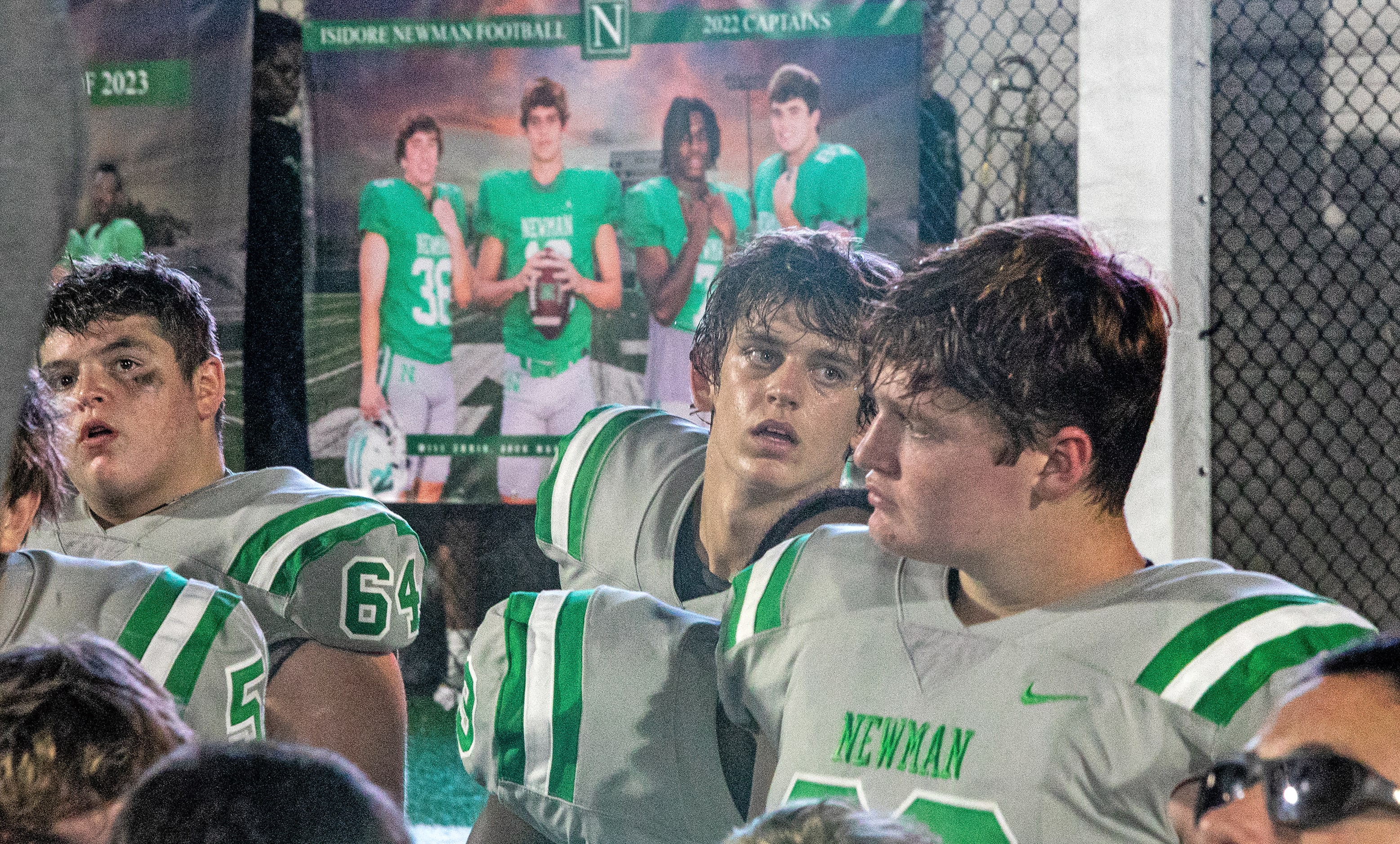 Arch Manning kneels with teammates for a post-game talk with a team poster over his shoulder...