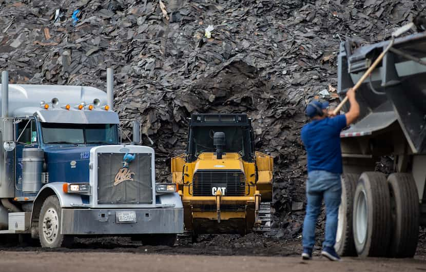 Workers prepare to haul off the mountain of roofing shingles at "Shingle Mountain" at Blue...