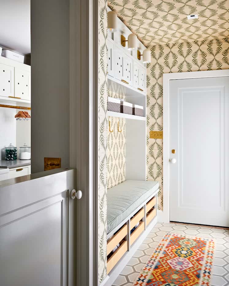 In a mudroom, a bench offers storage beneath it and a colorful, patterned wallpaper is a...