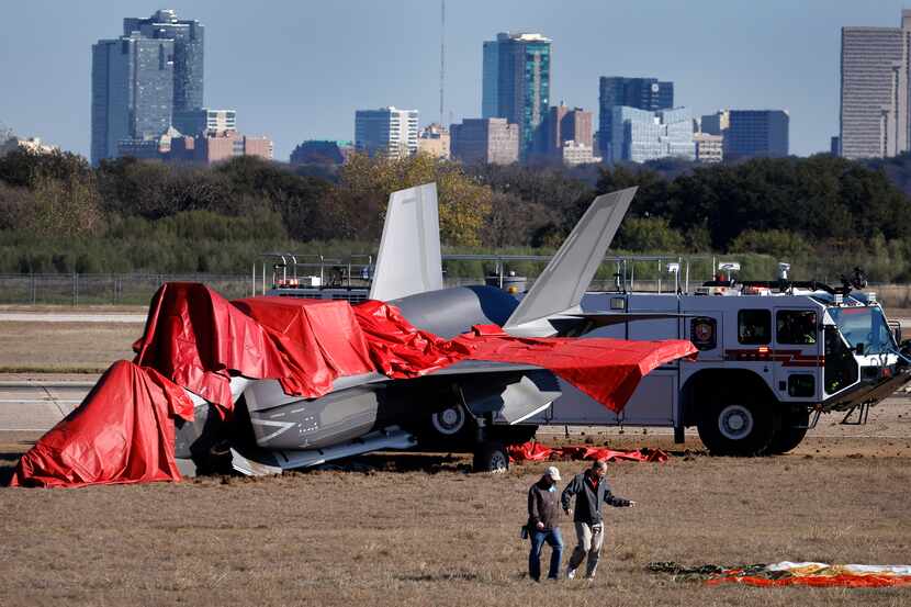 Officials look over the F-35B military aircraft wreckage, including the parachute (right)...