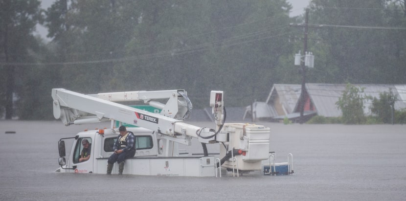 Men wait on a utility vehicle that was stuck on Highway 96 in flood waters from Hurricane...