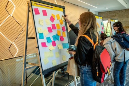 A teenage girl wearing a backpack stands facing a large interactive easel covered with...