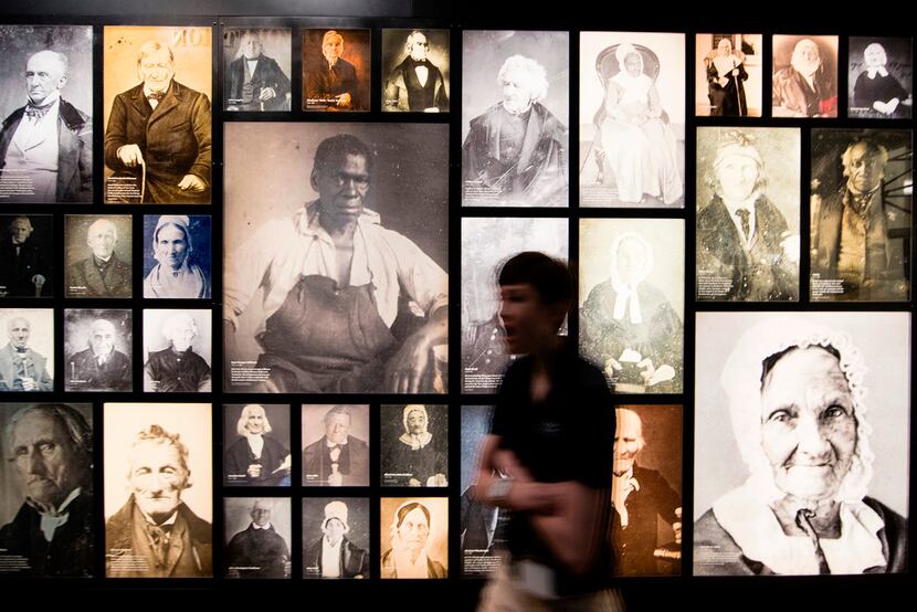 A museum patron walks  past a wall of portraits at the Museum of the American Revolution in...
