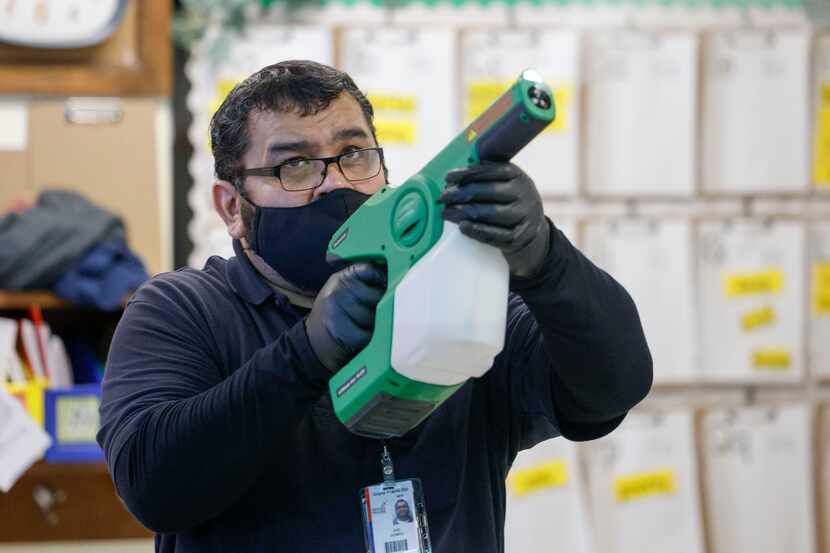 Custodian Joe Gomez, who lives with his elderly parents, sprays disinfectant in a classroom...