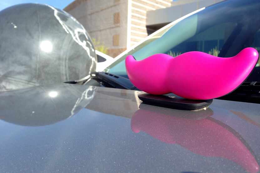 The signature pink mustache of ride-booking company Lyft sits on the hood of a vehicle...