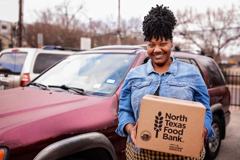 A woman holds a cardboard box that reads North Texas Food Bank in front of a maroon car.