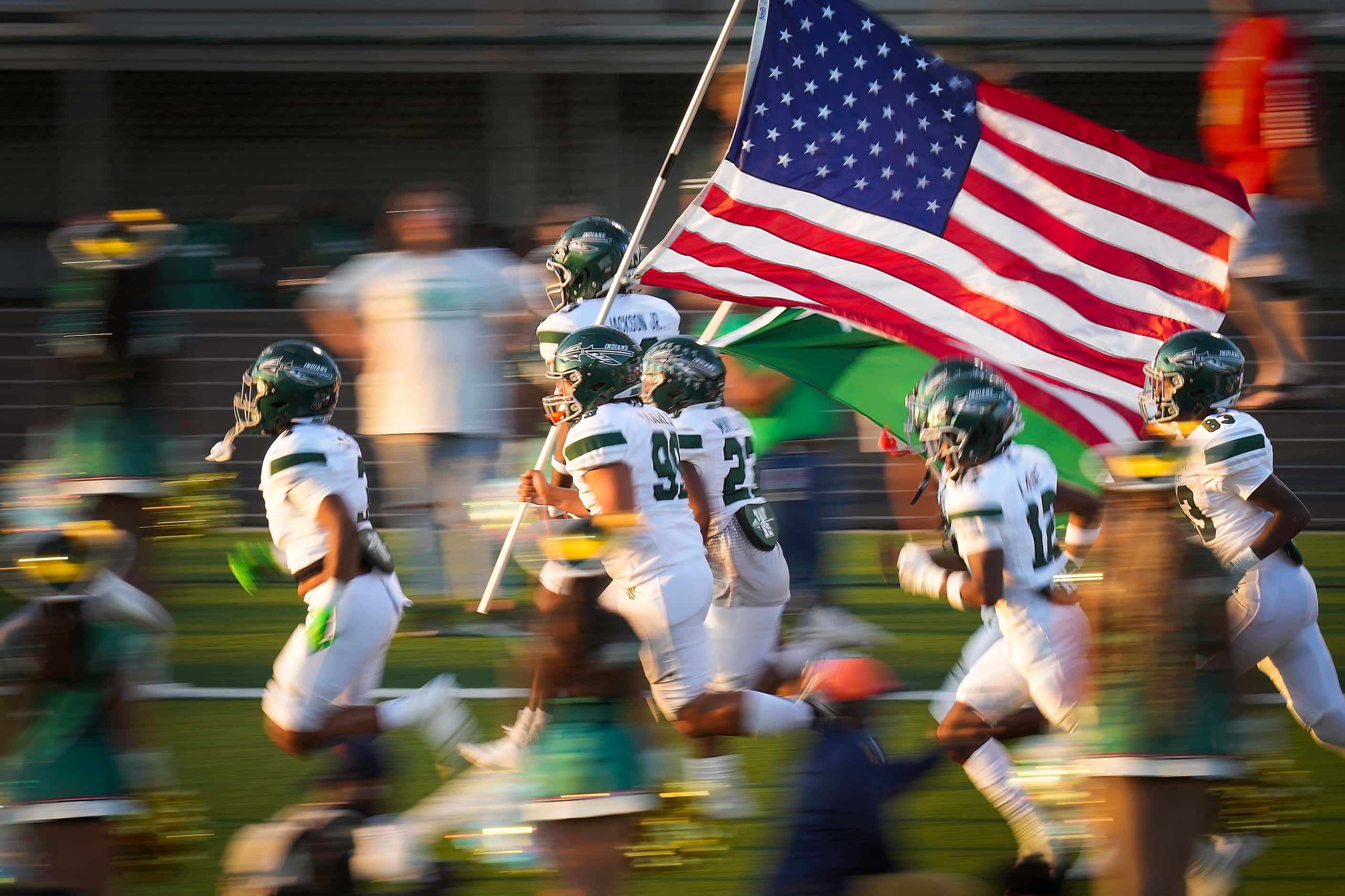 Waxahachie players carry the American flag as they take the field before a high school...