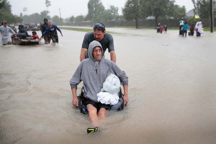 People make their way out of a flooded neighborhood after it was inundated with rain water,...
