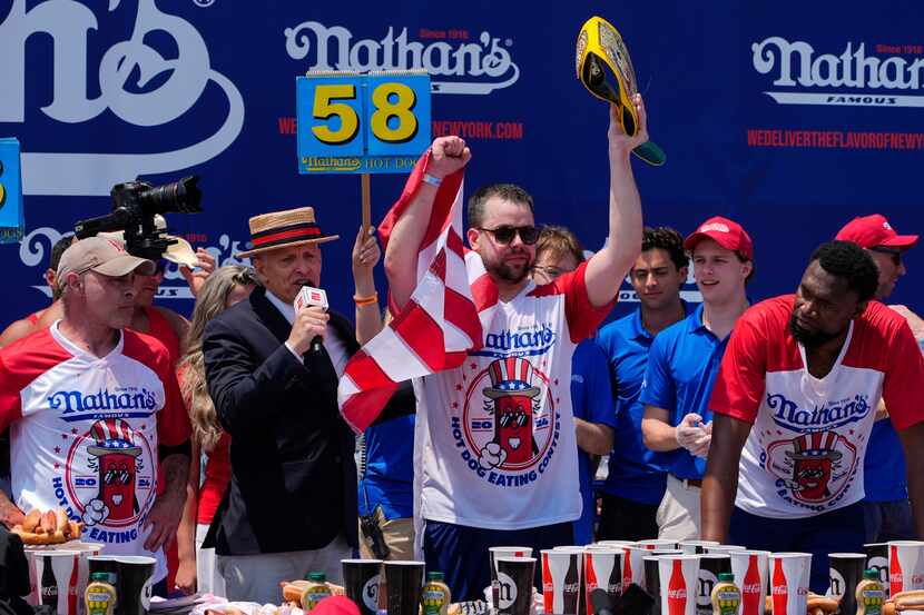 Patrick Bertoletti (center) reacts after winning the men's division in Nathan's Famous...