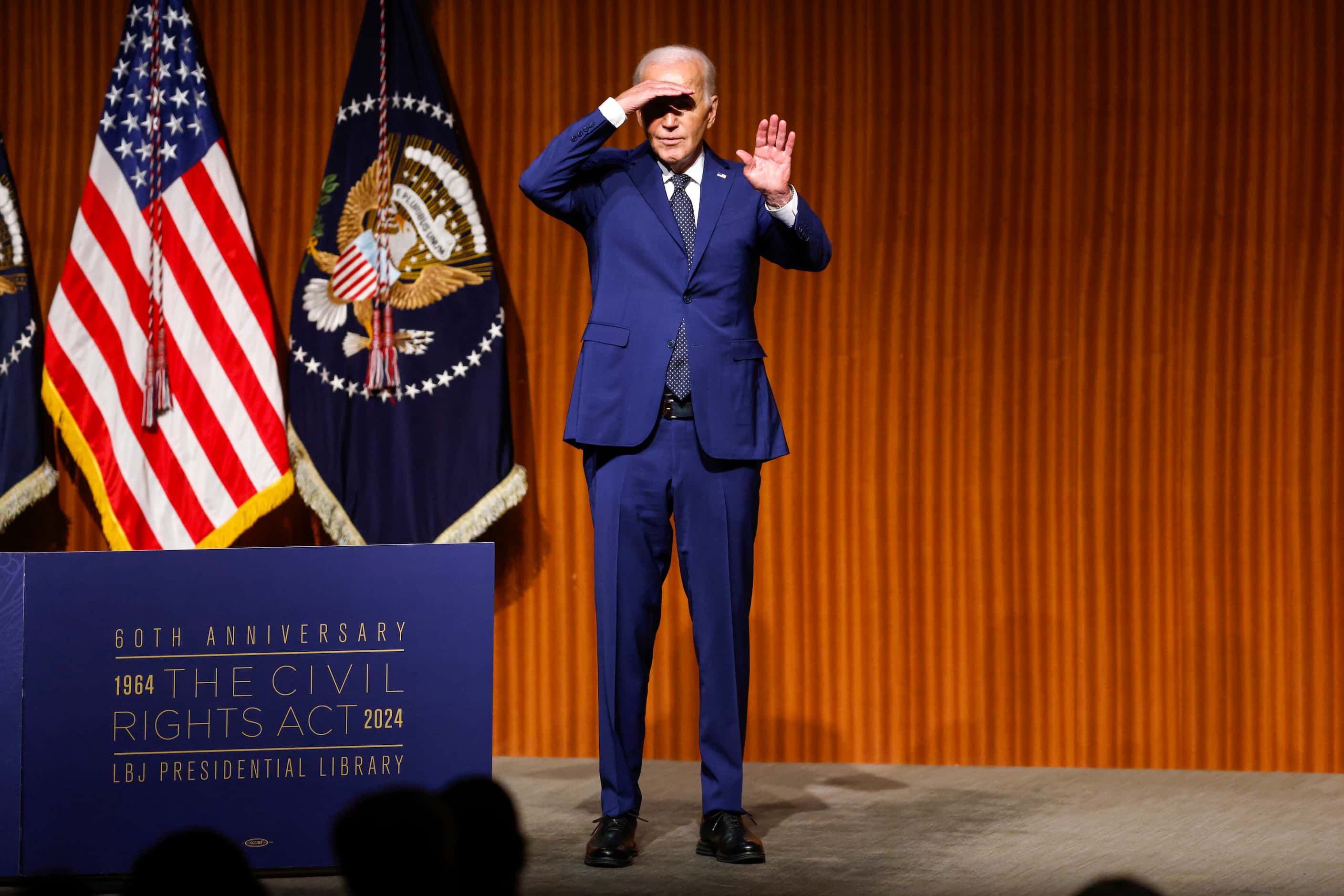 President Joe Biden shields his eyes from the stage lights to wave at attendees after...