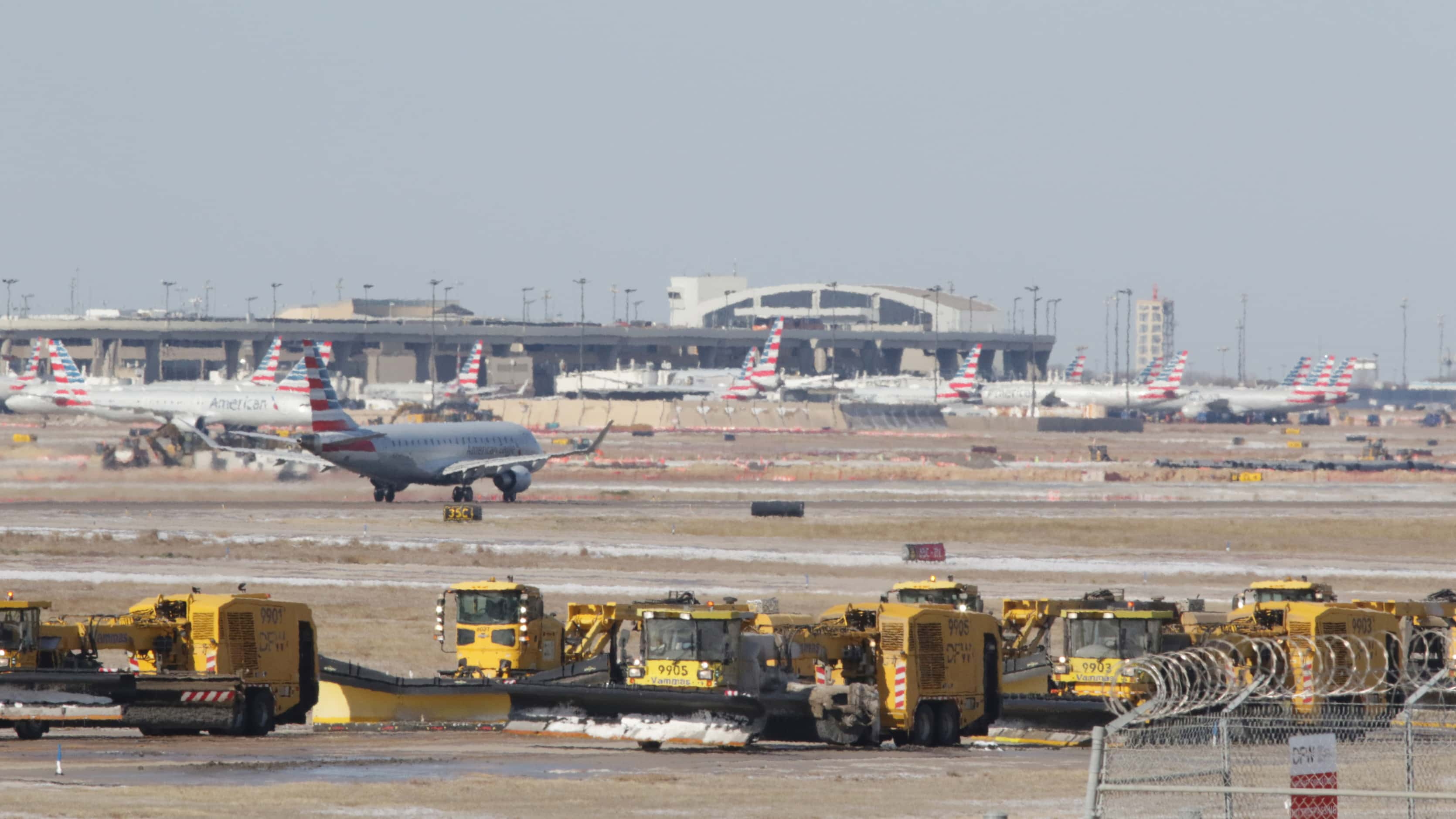 Snow plowers sit on the side of  a runway as an American Airlines jet takes off at Dallas...